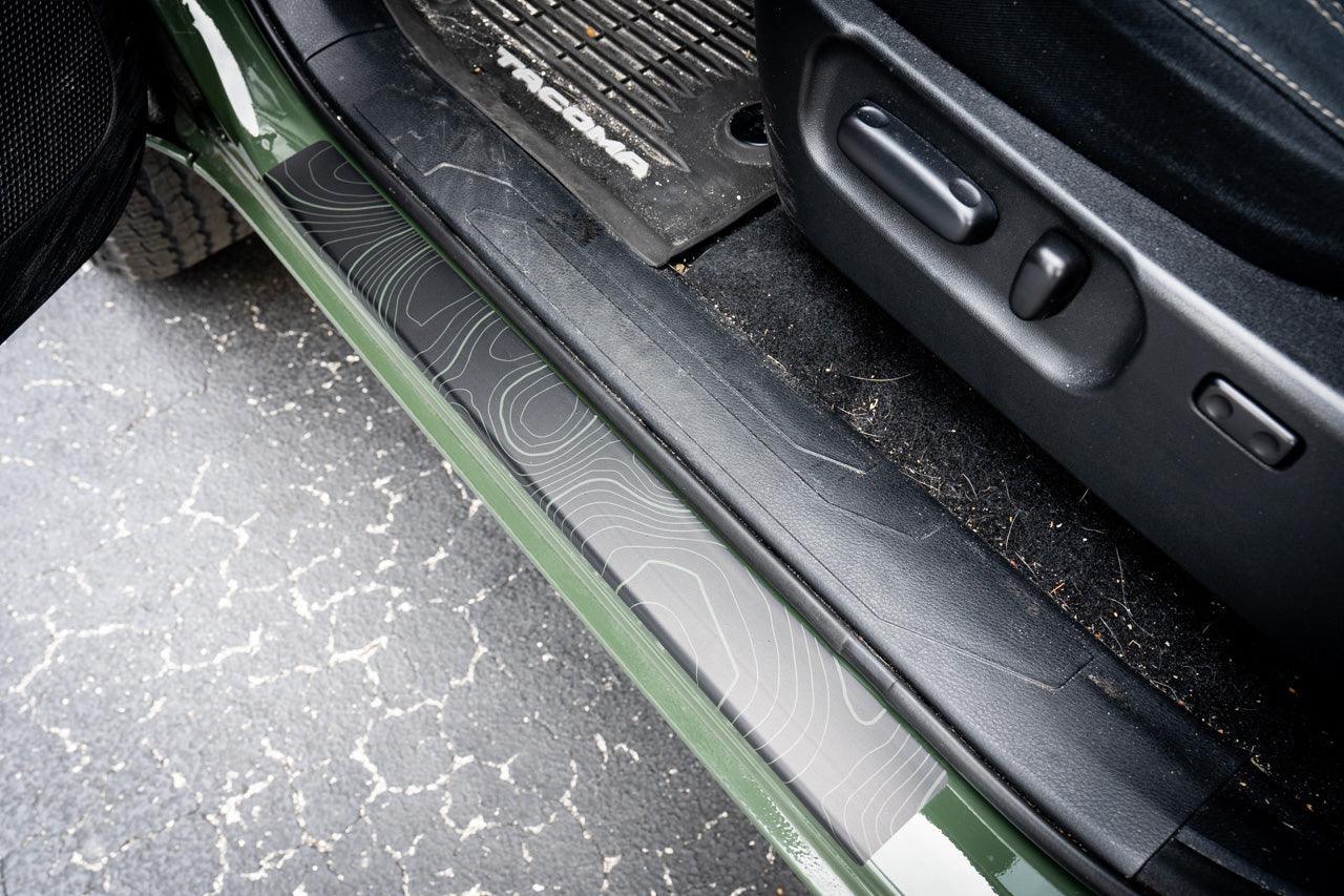 StickerFab Topo Door Sill Protectors for 2016-2023 Tacoma Double Cab, showing textured black door sill guards on vehicle door frame.