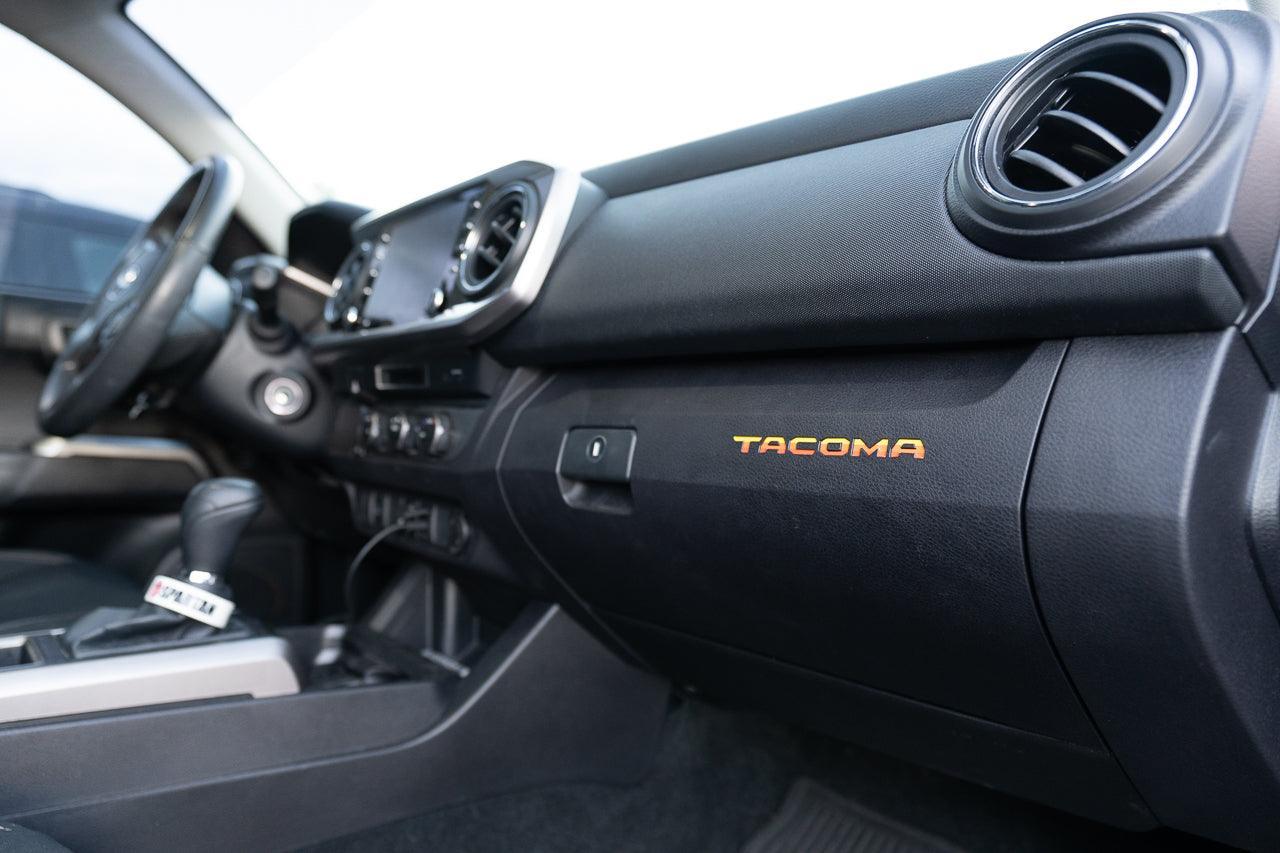 Vinyl glove box logo inlays for 2016-2023 Toyota Tacoma interior, printed series by StickerFab, featuring Tacoma branding.