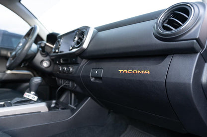 Vinyl glove box logo inlays for 2016-2023 Toyota Tacoma interior, printed series by StickerFab, featuring Tacoma branding.
