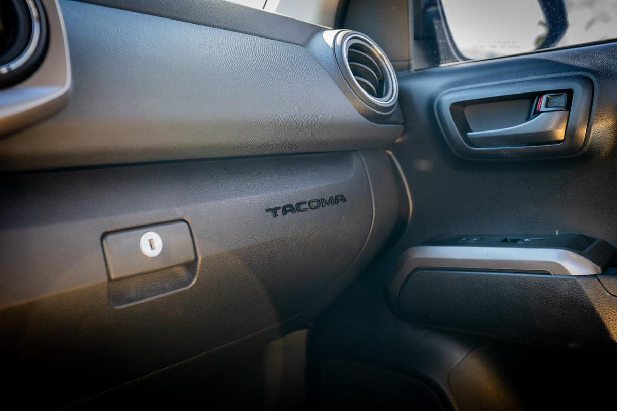 A close-up of a 2016-2023 Tacoma glove box with acrylic "TACOMA" logo inlays featuring laser-etched details.
