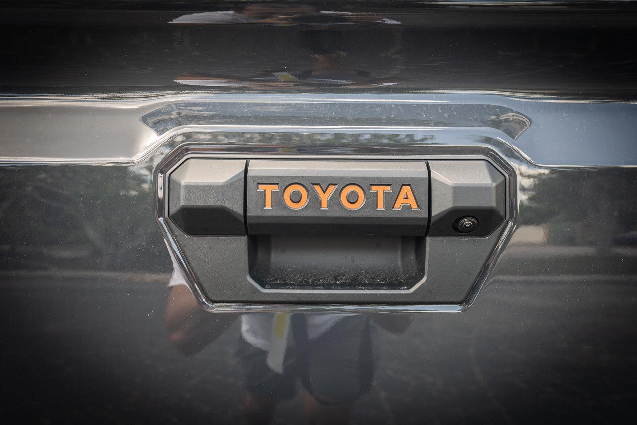 Tailgate handle inlay letters for 2024+ Toyota Tacoma, vinyl exterior decal by StickerFab, shown on vehicle tailgate.