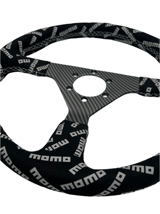 Black suede racing steering wheel with carbon center from Momo, designed for performance driving by Speedzone Performance LLC.