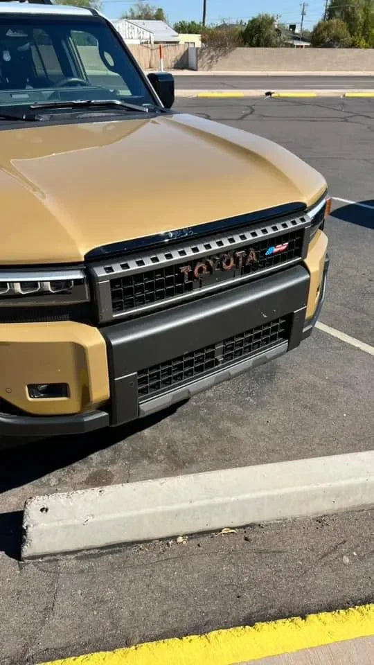 Toyota Topo front grille emblem kit for 2024+ Land Cruiser and 07-14 FJ Cruiser, shown on a vehicle's front grille.