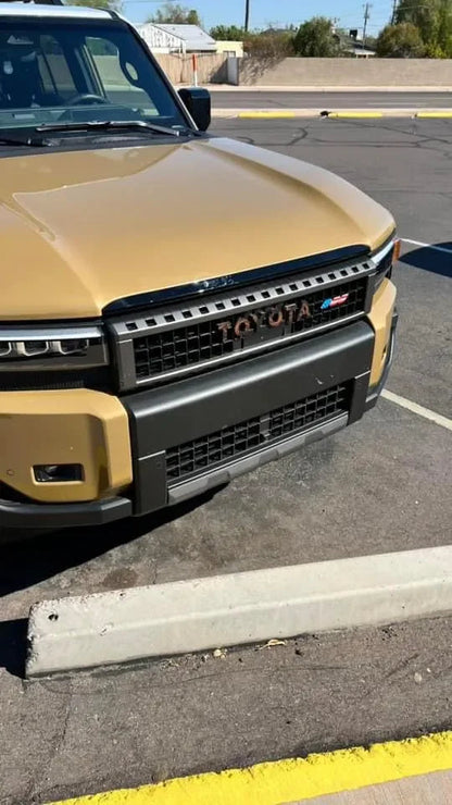 Toyota Topo front grille emblem kit for 2024+ Land Cruiser and 07-14 FJ Cruiser, shown on a vehicle's front grille.